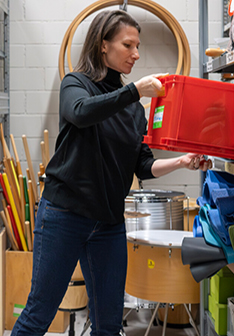 Sarah Keusch stellt eine rote Kiste auf ein Regal