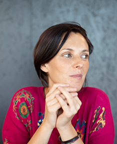 Porträtfoto von Francesca Verunelli, die nachdenklich zur Seite blickt. Sie trägt ein farbenfrohes Oberteil mit einem detaillierten Muster und stützt ihre Hände leicht ineinander gefaltet auf. Francesca Verunelli wird ab Frühlingssemester Dozentin an der Hochschule Luzern – Musik. 