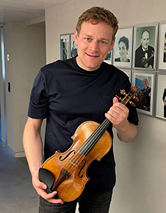 Sebastian Bohren hält seine Geige vor der Gallerie der Preisträger/innen