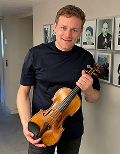 Sebastian Bohren hält seine Geige vor der Gallerie der Preisträger/innen