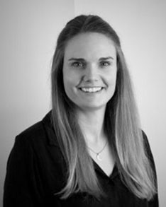 Smiling woman with long hair wearing a blazer in a black-and-white portrait against a light background.