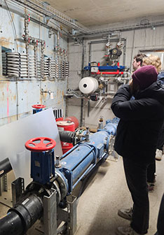 Studierende in einem Technikraum mit Pumpensystem, Ventilen und Steuerung einer Heizungsanlage im Bereich Gebäudetechnik.