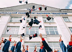 Foto zeigt eine  Gruppe Absolvent*innen, die ihre Hüte in die Luft werfen.