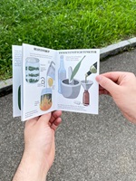 Eine Ausstellungstafel und verschiedene Illustrationen über Wildkräuter, insbesondere Spitzwegerich, Löwenzahn, Brennnessel und Bärlauch. Die Gestaltung kombiniert detailreiche Schwarz-Weiss-Skizzen und farbige Illustrationen, ergänzt durch erklärende Texte. Im Vordergrund ein Faltheft in der Hand, das mit klaren Grafiken den praktischen Gebrauch der Pflanzen darstellt.
