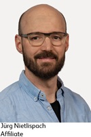 Porträt von Jürg Nietlispach. Jürg hat eine Halbglatze, einen dunkelbraunen Bart und trägt eine Brille.