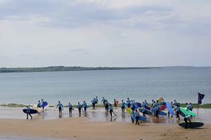 Studierende am Strand auf dem Weg ins Meer mit Surfboards