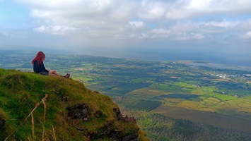 Zwei Studierende sitzen auf einem Vorsprung eines Berges und sehen in die Weite