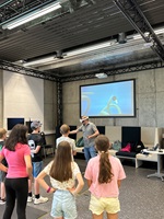 Eine Gruppe Kinder schaut einem Mann mit VR-Brille bei einer Demonstration zu