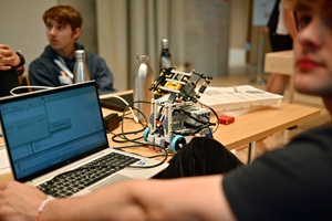 Ein junger Mann sitzt an einem Tisch mit einem Computer und einem Lego-Roboter