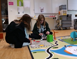 Zwei Mädchen sitzen am Boden und programmieren einen Lego-Roboter