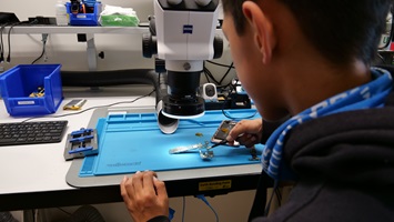 Ein baut mit einer Pinzette ein Mobiltelefon auseinander