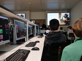 Kinder schauen in einem Unterrichtszimmer auf einen grossen BIldschirm