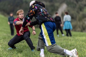 Zwei junge Menschen tanzen in der Natur auf einer Wiese. Im Hintergrund sind weitere Menschen verschwommen erkennbar. 