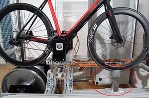 Das Bild zeigt ein im Prüfstand eingespanntes e-Bike. Das Fahrergewicht wird über den rot markierten Zylinder eingestellt.