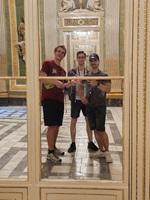 Drei Besucher posieren vor einem Spiegel in einem prunkvoll ausgestatteten historischen Innenraum.