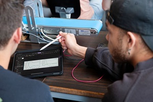 Students analyze measurement data on a tablet next to a technical test setup