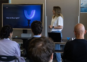 Presentation on blue light technology with mouthpiece displayed on screen to seated audience