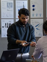 Student demonstriert ein elektrisches Zahnpflegegerät vor Designskizzen im Seminarraum