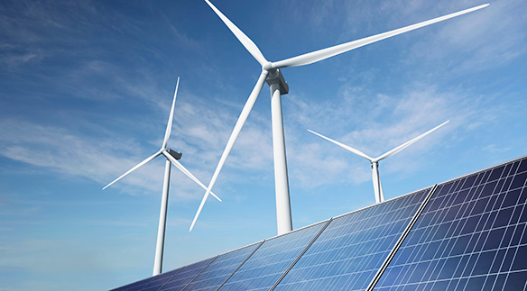 Foto zeigt drei Windräder, im Vordergrund ist ein Teil von einer Solarpanelanlage erkennbar.