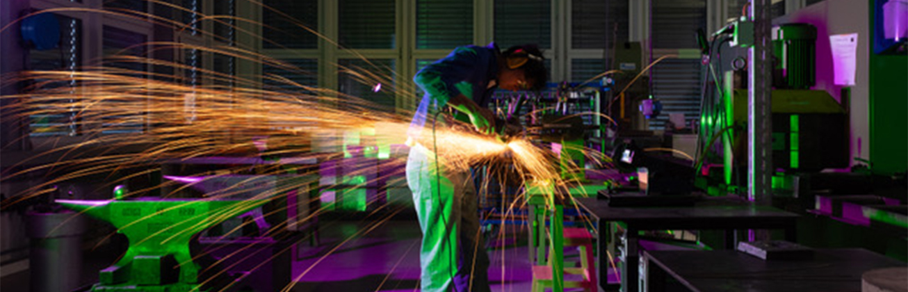 Mann in einer Metallwerkstatt, die Funken sprühen. 