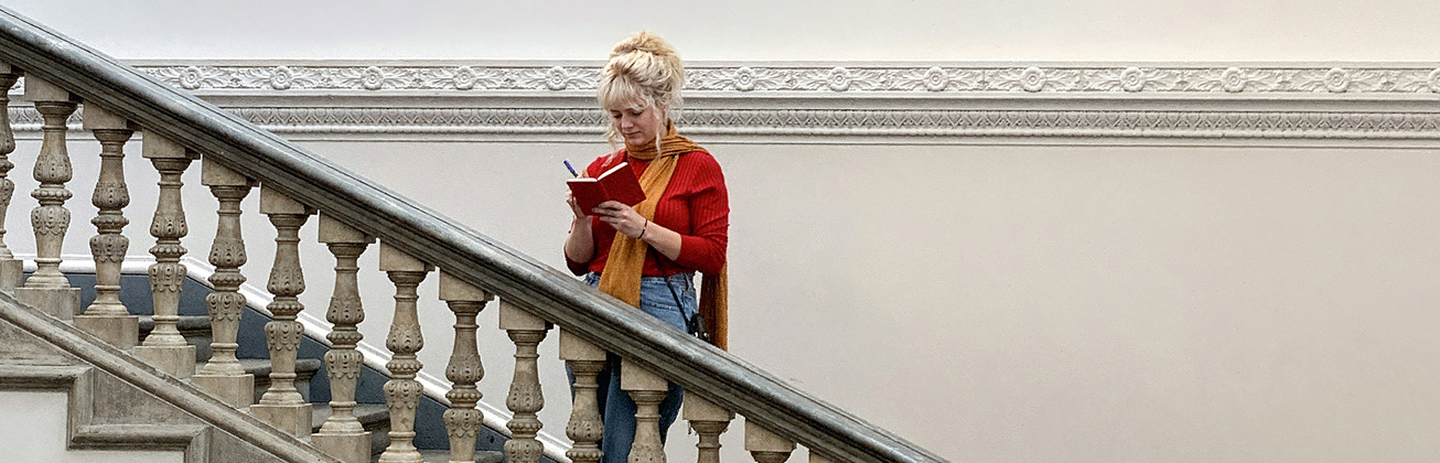 Studentin steht auf der Treppe und schreibt in ihr Notizbuch