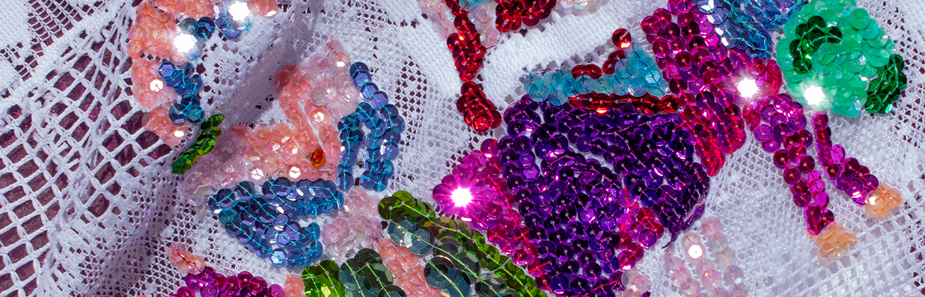 Ein weisser Stoff mit farbig-glitzernden Paletten bestickt, die eine Libelle darstellen. 