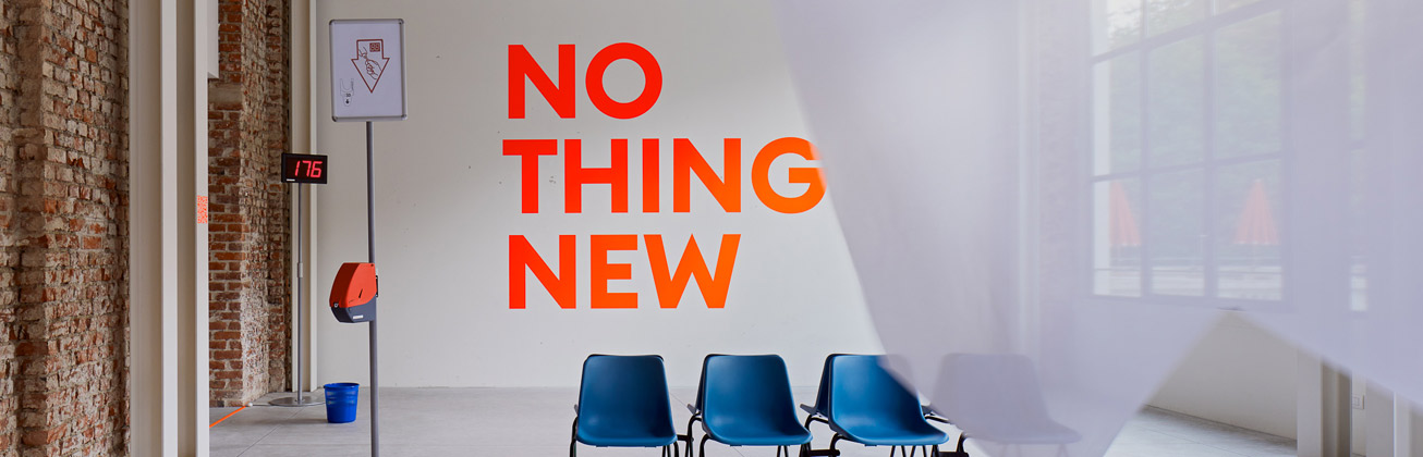 Eine insustrielle lichtdurchflutete Halle, in der vier blaue Plastikstühle stehen und an der Wand steht gross in Neon-orange: 