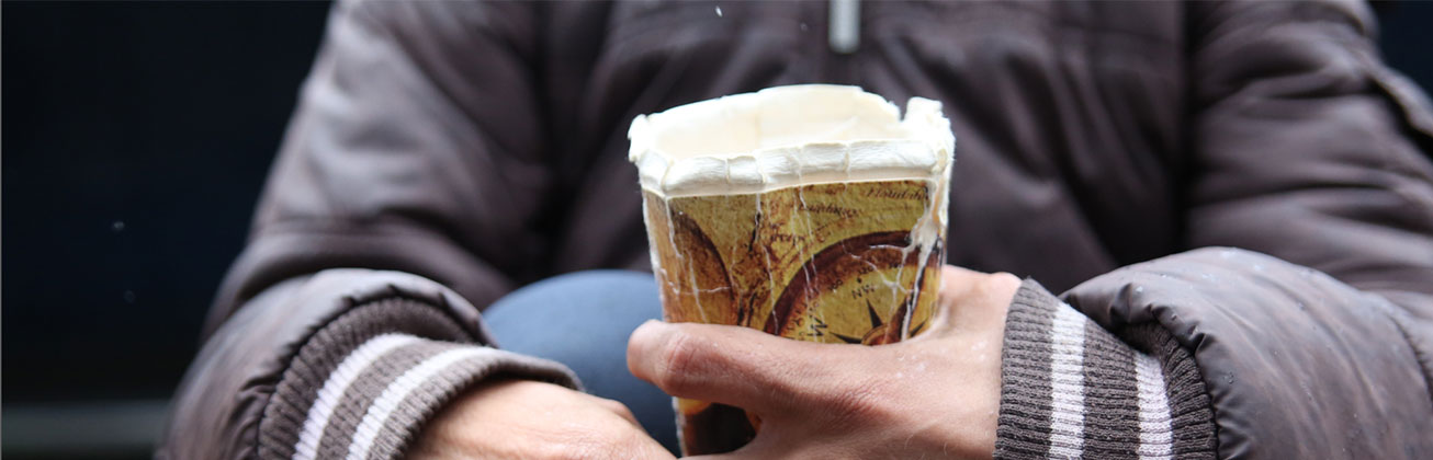 Händen, die einen kaputten Pappbecher halten