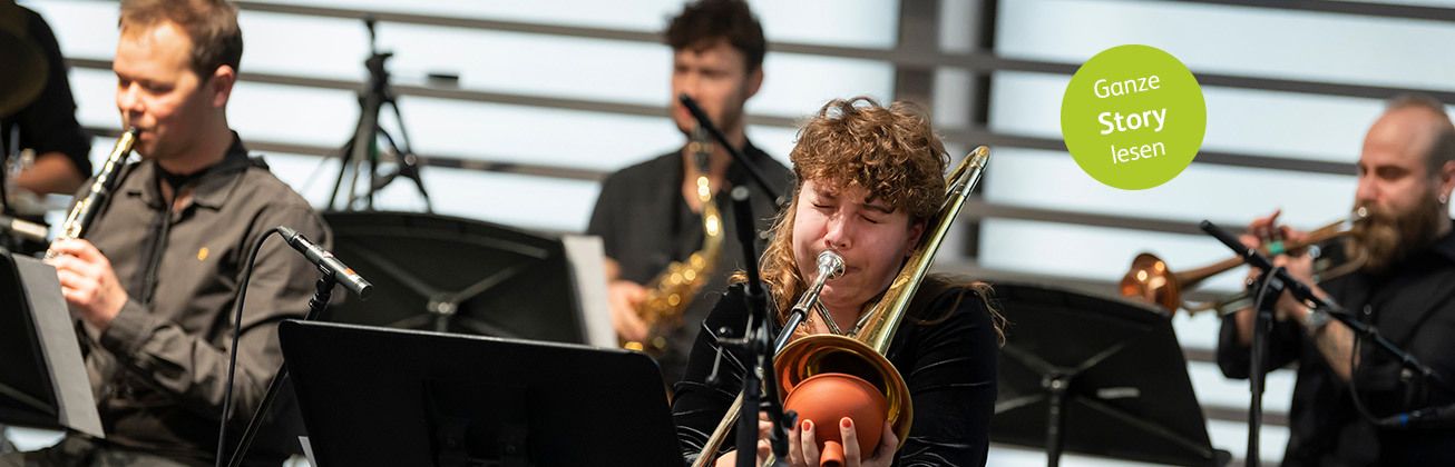 Blechbläser und - bläserinnen beim Musizieren an einem Konzert, die Vorderste von ihnen spielt mit geschlossenen Augen leidenschaftlich Posaune