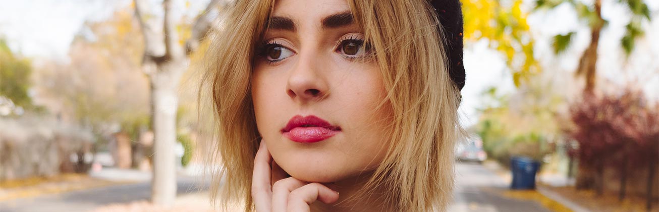 Studentin befindet sich in der herbstlichen Natur und blickt nachdenklich nach Links, dabei stützt sie ihr Kinn sanft auf ihren Fingern ab