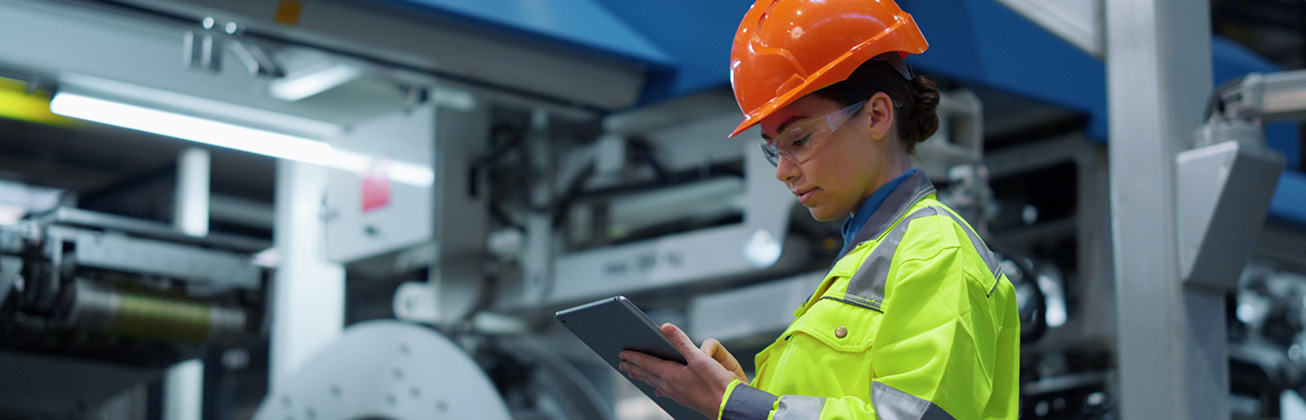 Ingenieurin schaut auf ein Tablet in einer modernen Maschinenfabrik