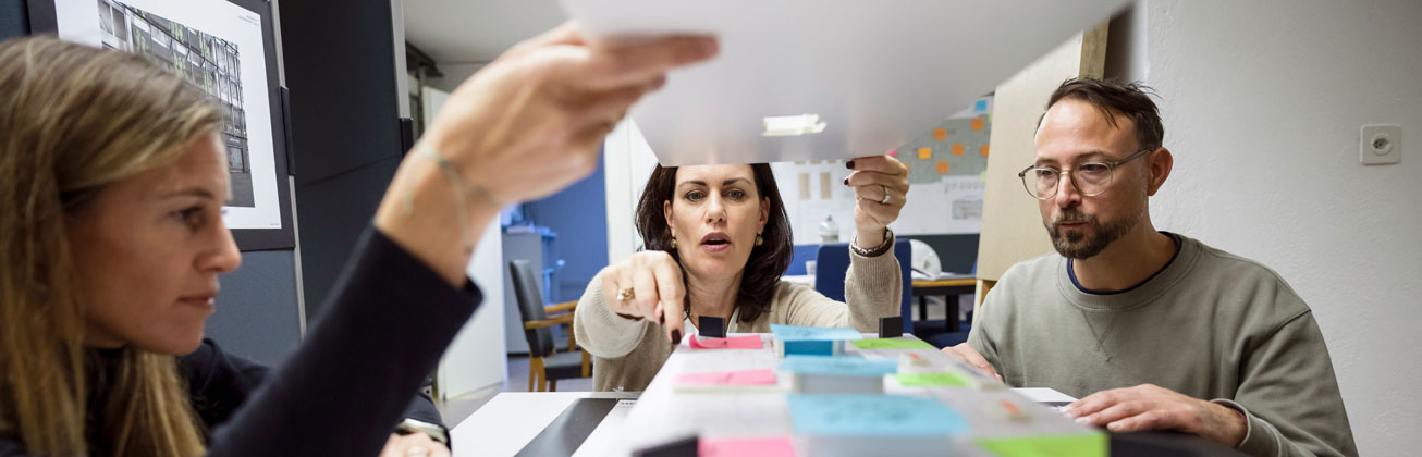 Zwei Frauen und ein Mann sitzen um einen Tisch mit Post-Its