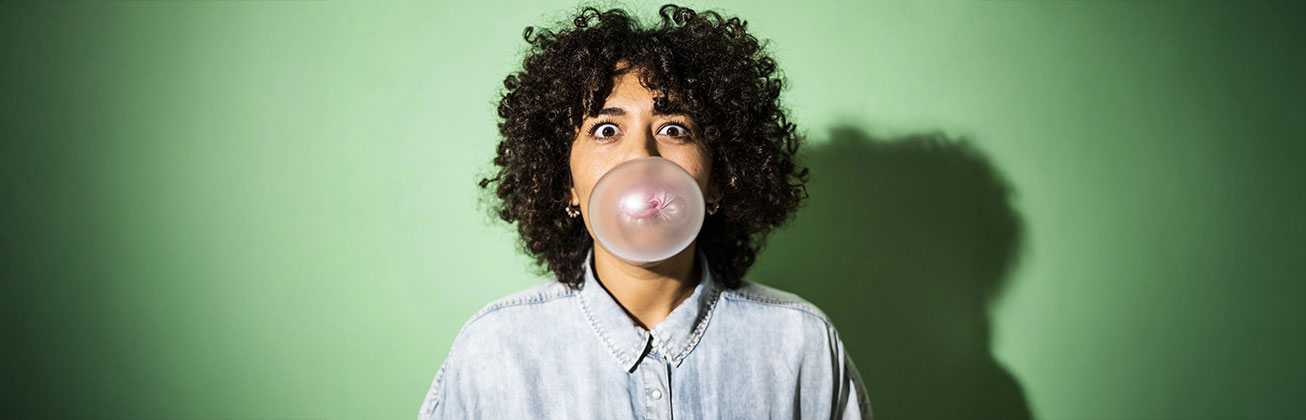 Frau mit Lockenkopf macht Kaugummi-Blase auf grünem Hintergrund