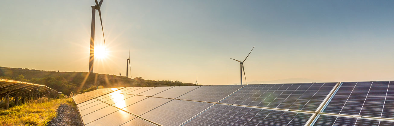 Windräder und Solarpanels in Landschaft bei Sonnenuntergang
