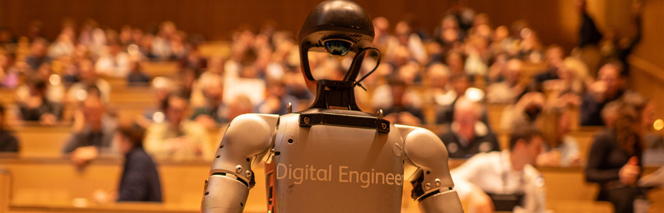 Ein Humanoid steht vor einer Gruppe von Menschen in einem Hörsaal