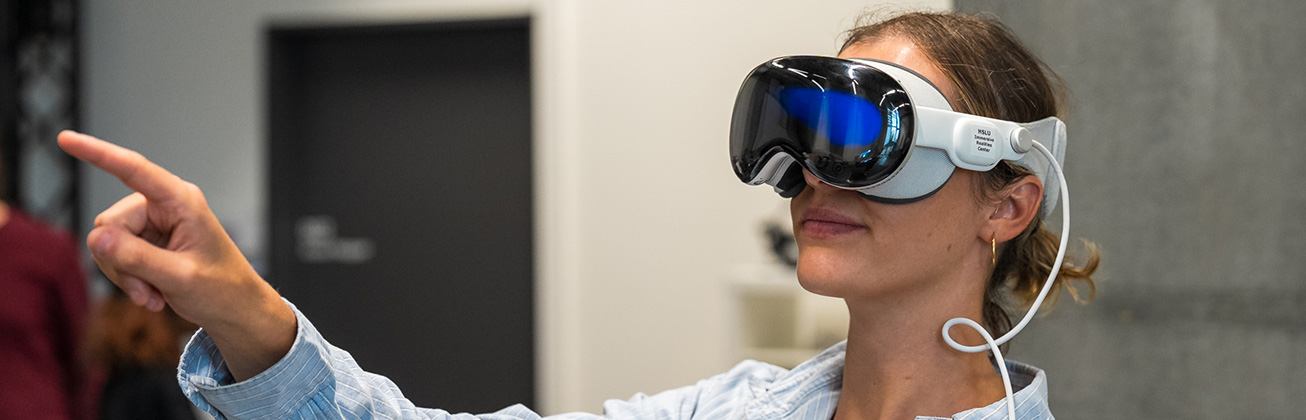 Eine junge Frau trägt eine VR-Brille und zeigt in die Luft