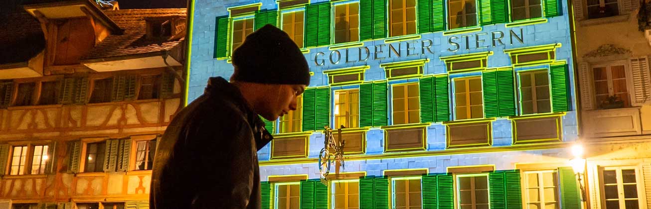 Zwei Studierende beleuchten eine Hauswand mit einem Beamer