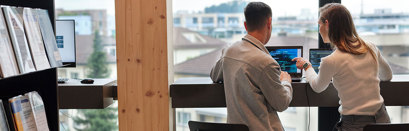 Zwei Studierende sitzen an einer langen Theke mit Blick aus einem grossen Fenster auf eine Stadtlandschaft