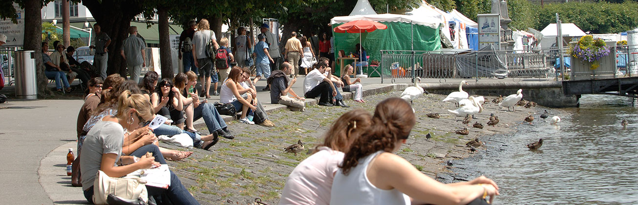 Menschen sitzen in Luzern am Ufer des Vierwaldstättersees.