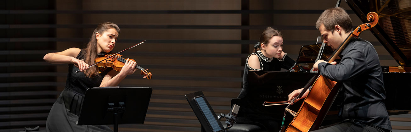 Student lehnt sich an einer Wand und spielt sitzend Gitarre.