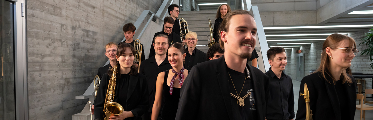 Die junger Musikerinnen und Musiker der HSLU Big Band mit Blasinstrumenten, die lächelnd eine Treppe hinuntergehen.