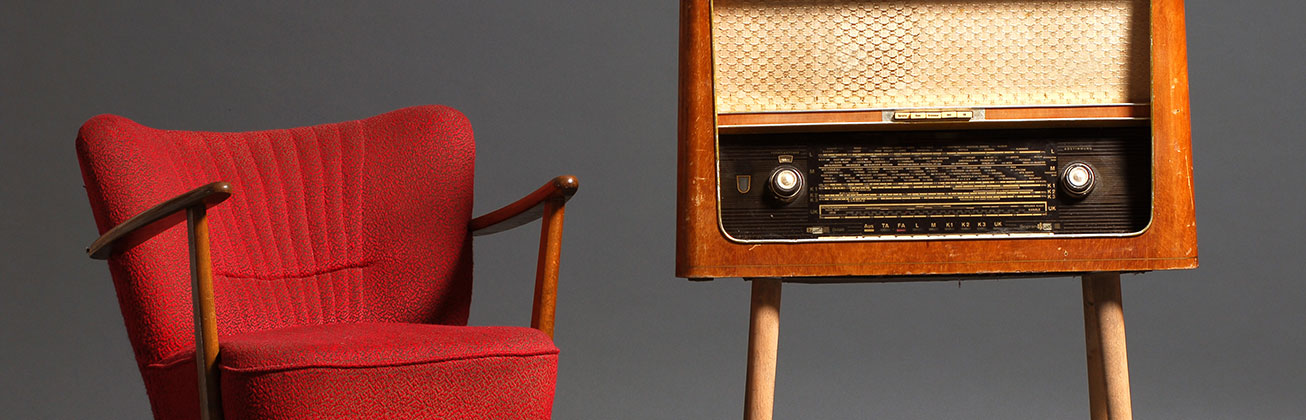 Symbolbild. Ein roter Sessel steht neben einem Radioschrank im Stil der 50er-Jahren. 