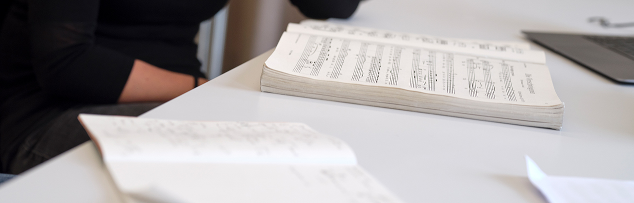 Person sitzt an einem Pult und studiert Musiktheorie aus einem Notenbuch.