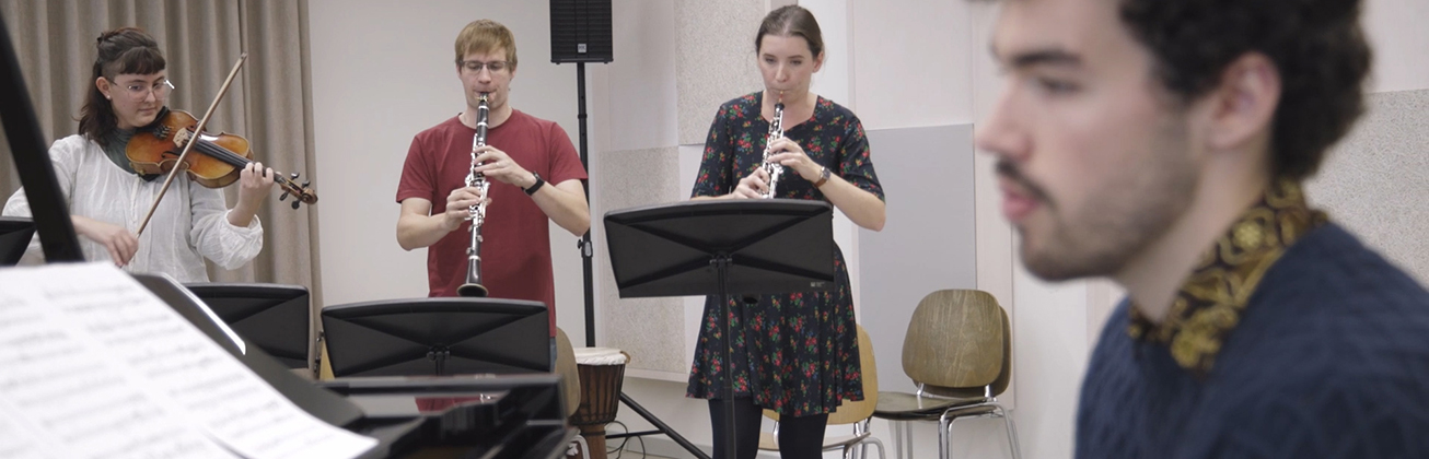 vier Musikstudierende sind in einem Unterrichtsraum mit verschiedenen Instrumenten zusammen am Musizieren
