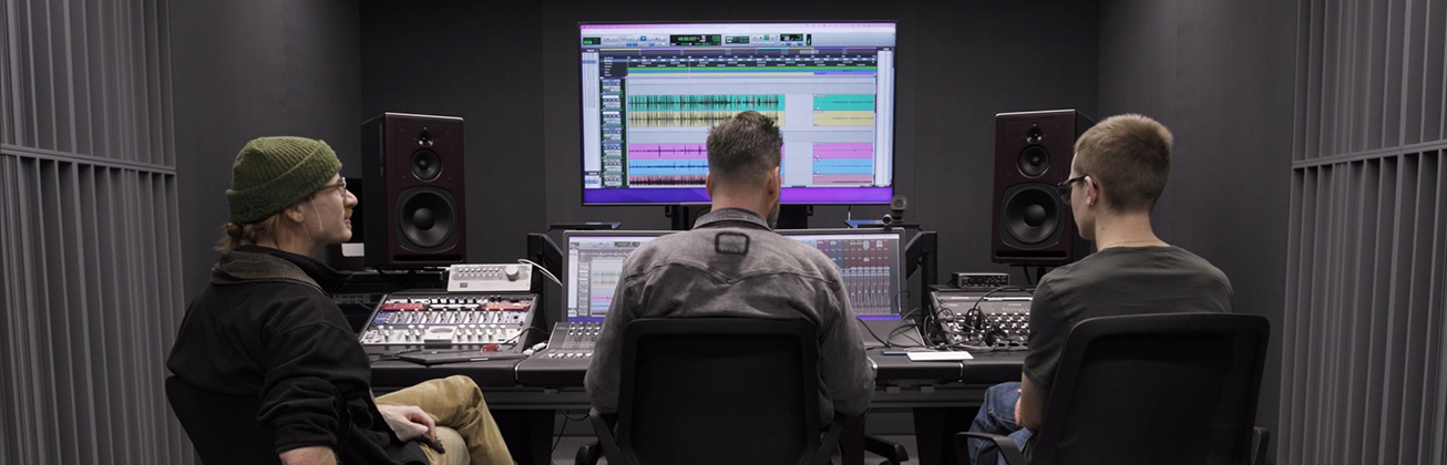 Tonstudio an der HSLU Musik mit drei Personen vor Mischpult und Bildschirm mit Audio-Software, umgeben von Lautsprechern und schallisolierten Wänden.