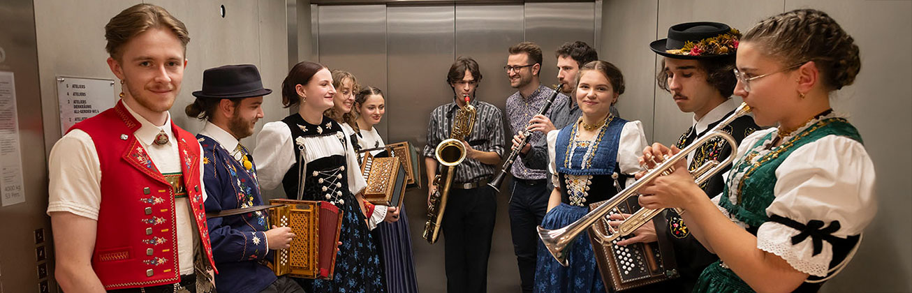 Junge Musiker und Musikerinnen in traditioneller Schweizer Kleidung, die verschiedene Instrumente, darunter schweizerische Traditionsinstrumente, in einem Lift halten.
