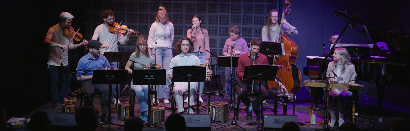 Ein Volksmusik-Ensemble mit jungen Musiker und Musikerinnen auf der Bühne, die teilweise auf traditionellen Schweizer Instrumenten spielen. 