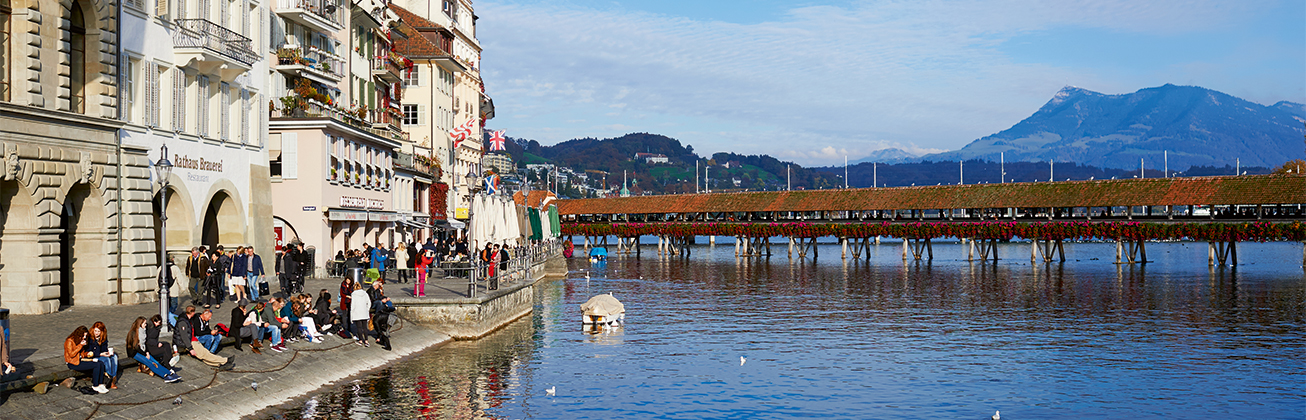 View of Lucerne’s Old Town with the Chapel Bridge and Lake Lucerne, set against a mountain backdrop.