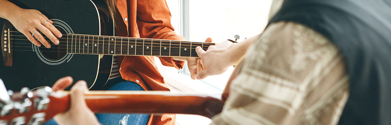 Ausschnitt zweier Personen im Gitarrenunterricht an einer Musikschule. 