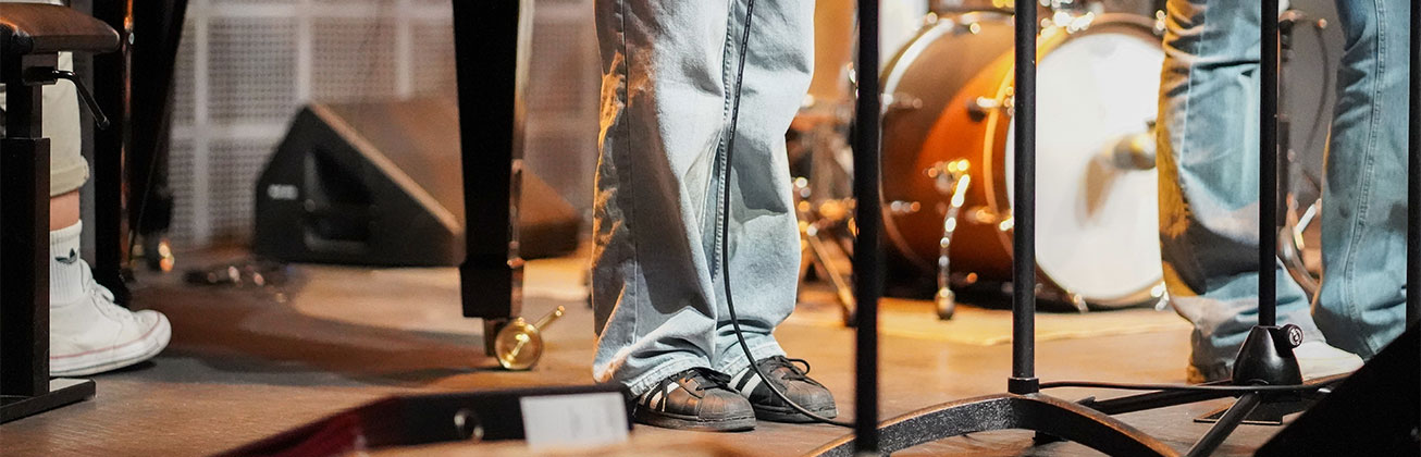 Beine von Musiker:innen auf einer Bühne mit Instrumenten im Hintergrund